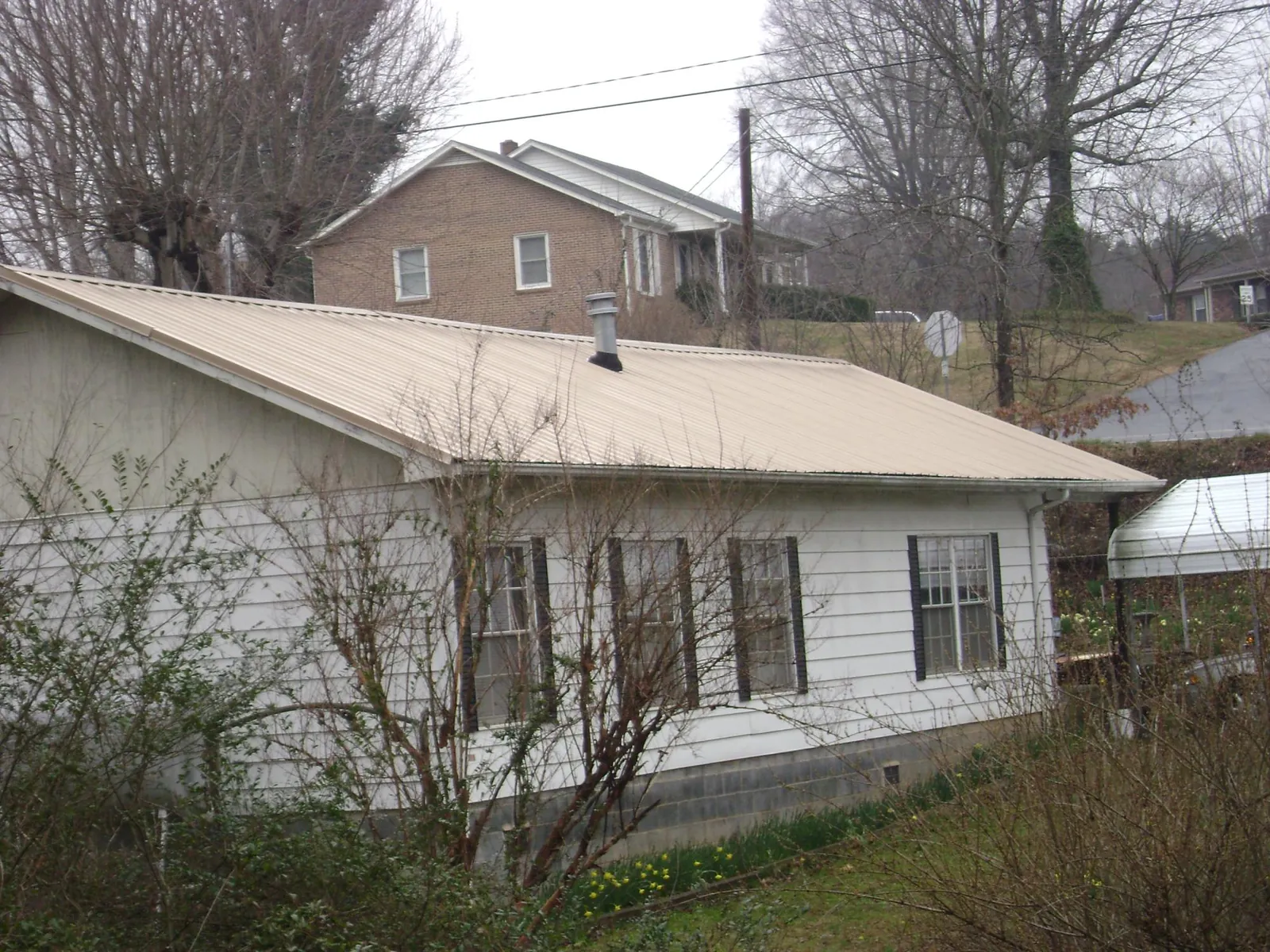 Tan metal roof on a white sided house set into a hillside — Commercial Roofing by Roofing Brothers in Clearwater